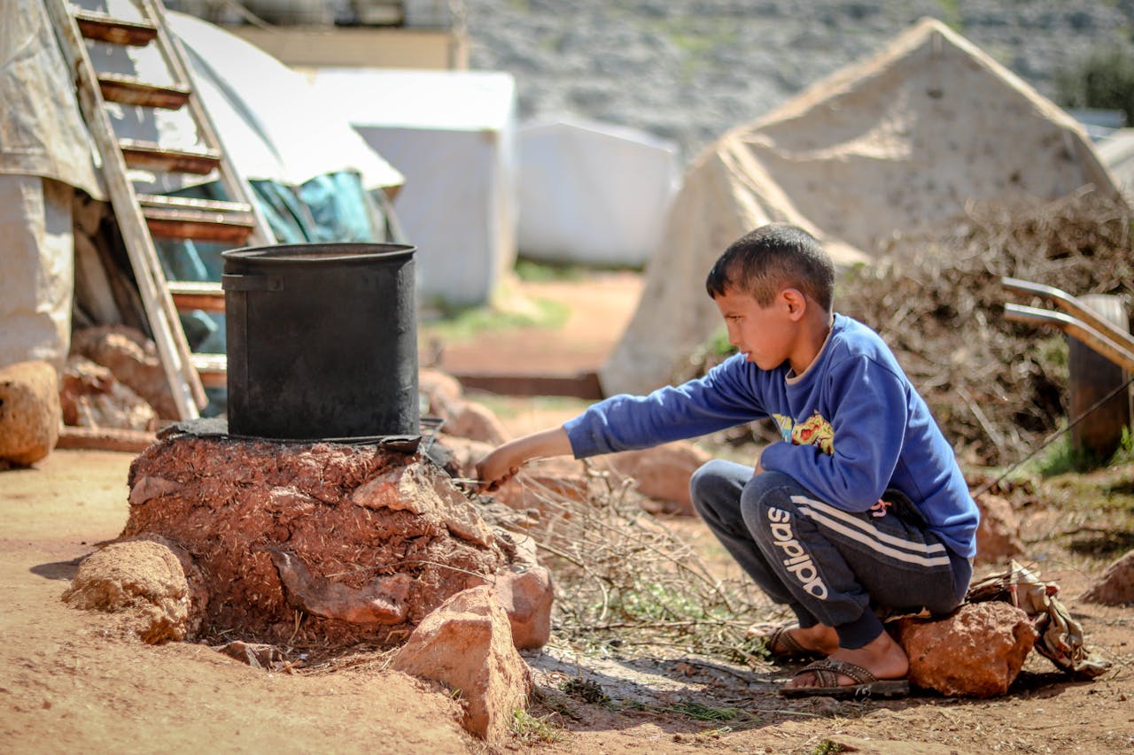 A young boy tends to a cooking pot outdoors in a refugee camp in Idlib, Syria.